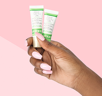 The White Tea & Citrus Satin Lips® Set is photographed in an African-American model’s pink-manicured hand in front of a two-toned pink background.