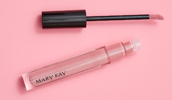 An open tube of shimmery pink Mary Kay® lip gloss is photographed alongside its doe foot applicator and a product smear.