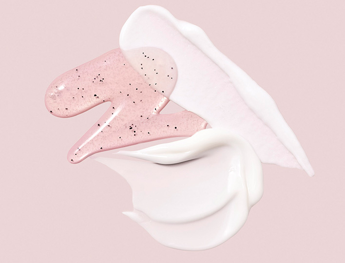 Muestras artísticas de productos exfoliantes Mary Kay® para el cuidado de la piel sobre un fondo rosa claro
