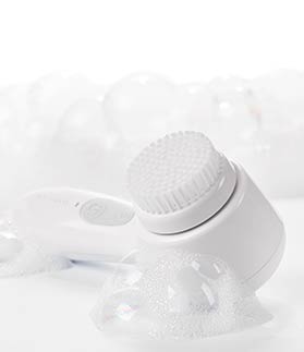 Skinvigorate Sonic™ Skin Care System de Mary Kay en posición horizontal junto a unas burbujas de jabón. 