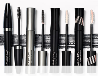A lineup of Mary Kay® mascaras with caps off showing wands and a smear of mascara in the background