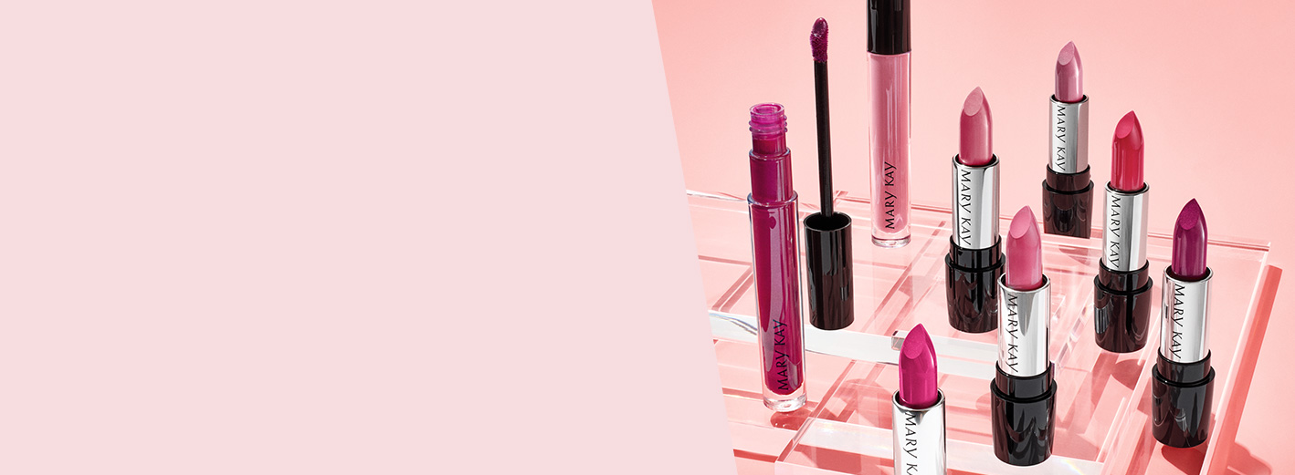 A group of Mary Kay® lipsticks and lip glosses on a pink background that are photographed together with caps off to show their beautiful colors