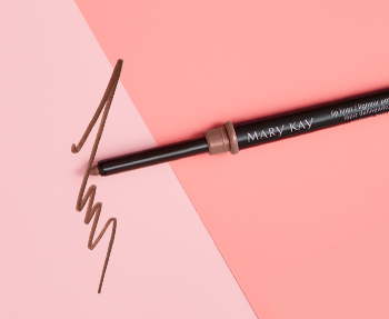 A Mary Kay® lip liner in a nude shade is photographed with its cap off atop a two-toned pink background and alongside a product smear.