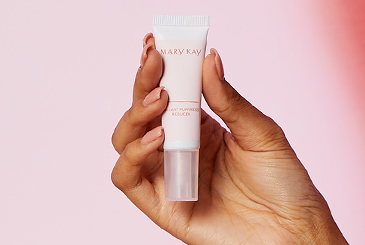 Hand holding a tube of Mary Kay® Instant Puffiness Reducer against a pink backdrop