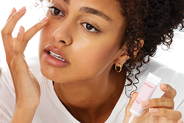 Close-up of female model touching the undereye area with her finger while holding a tube of Mary Kay® Instant Puffiness Reducer
