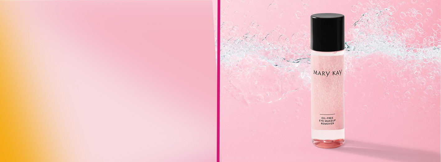 Botella del Mary Kay® Silkening Dry Oil de edición limitada junto al empaque exterior sobre carretes de listón contra un fondo de listones rosa