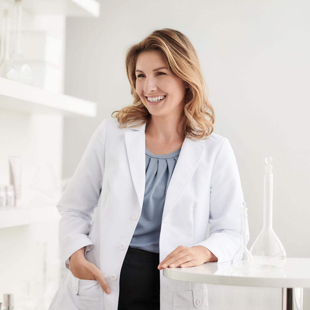 La Dra. Cristi Gomez, Directora de Seguridad de Productos y Toxicología Ambiental de Mary Kay, viste una bata blanca y apoya el brazo sobre una mesa.