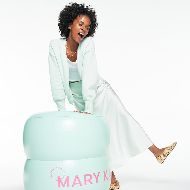 Woman sitting on giant green jar of Mary Kay Melt-In Cleansing Balm