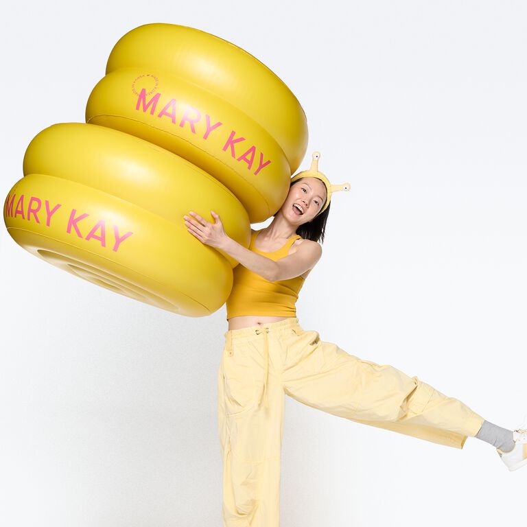 Woman hugging a stack of giant Mary Kay Snail Gel Face Patches jars