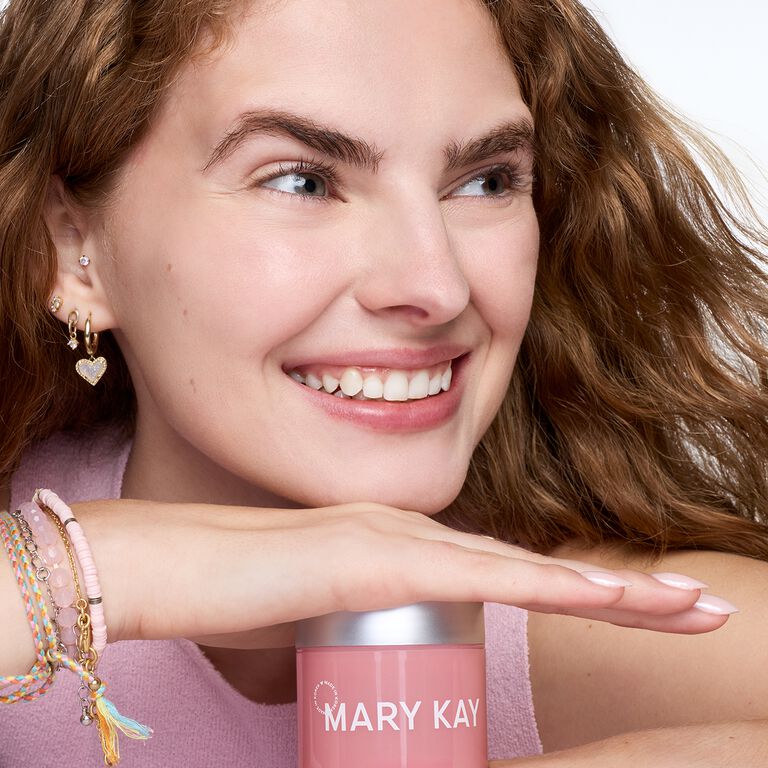 Una mujer sonriente descansa la mano y barbilla sobre frasco de Mary Kay Collagen Moisturizing Gel.