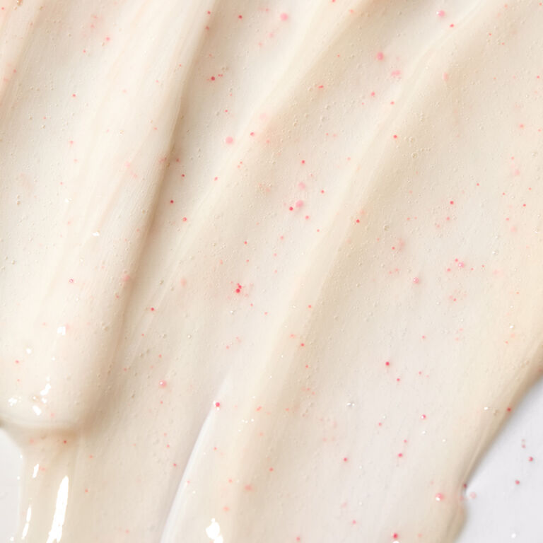 Close-up of a beige facial cleanser with small pink exfoliating beads spread in smooth strokes, showing product texture.