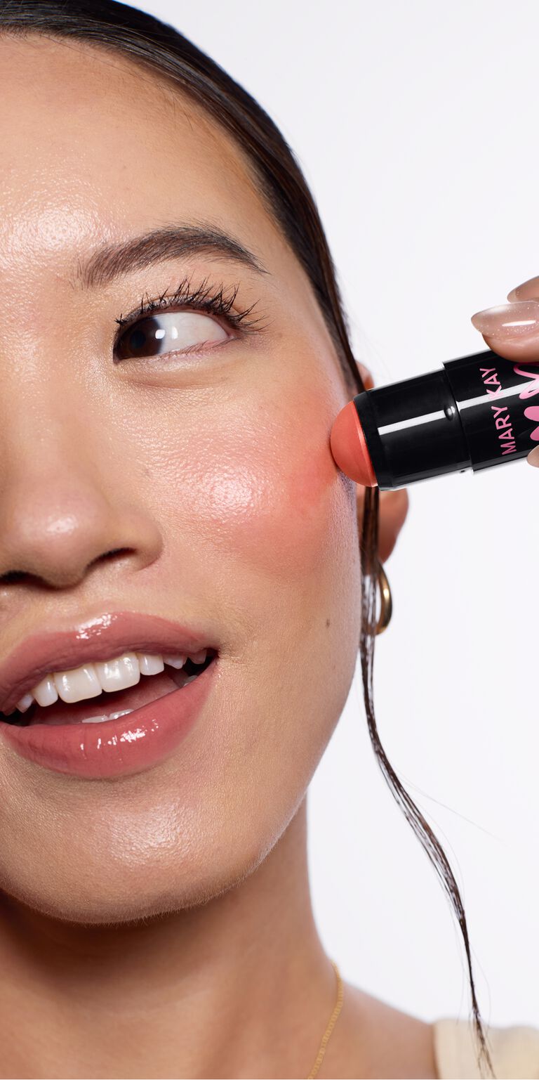 Model applies limited-edition Mary Kay Blush Stick in Spark Change to her  cheek while looking to the side