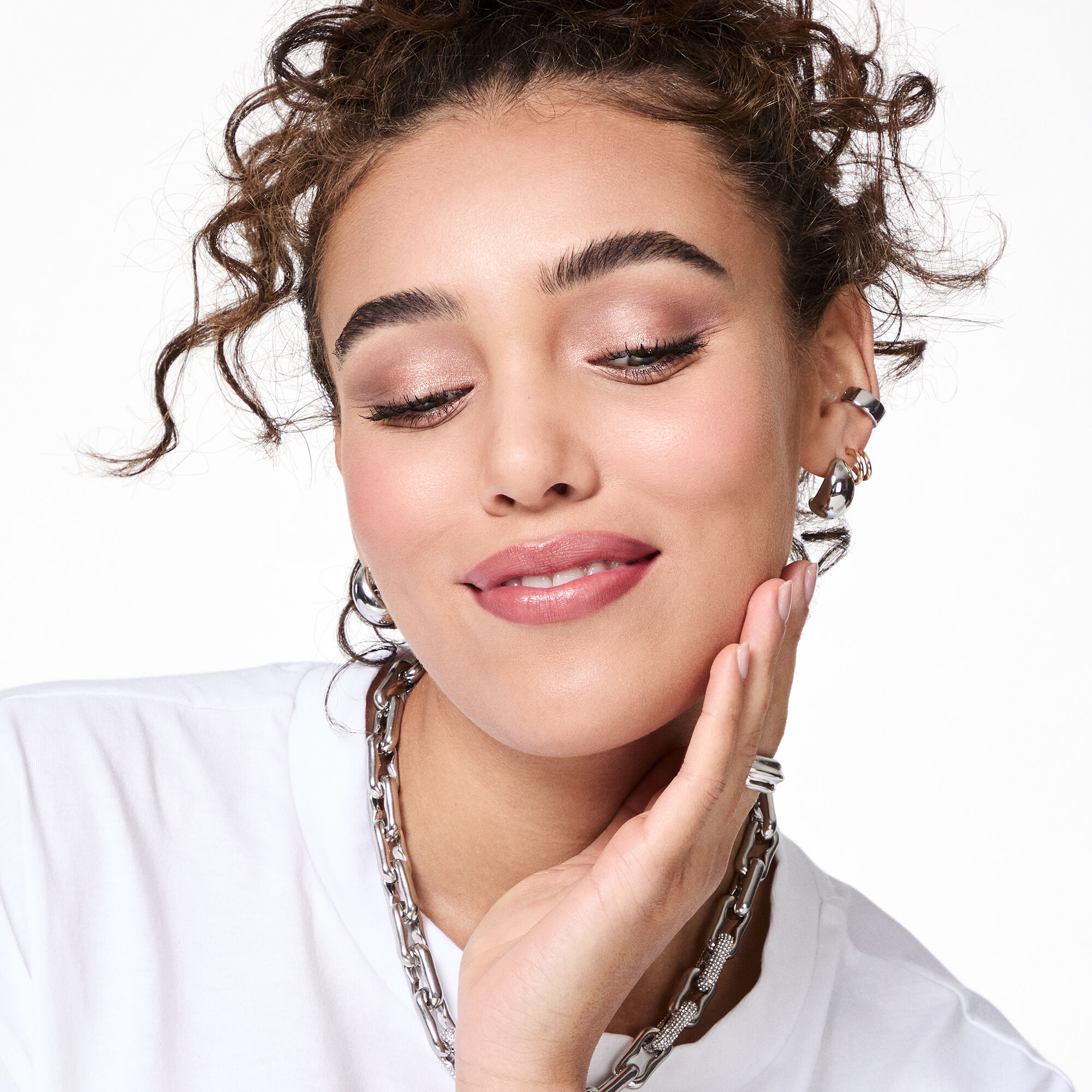 Una modelo casta&ntilde;a con cabello rizado que lleva el look All Eyes on Hue sonr&iacute;e suavemente mientras mira hacia abajo.