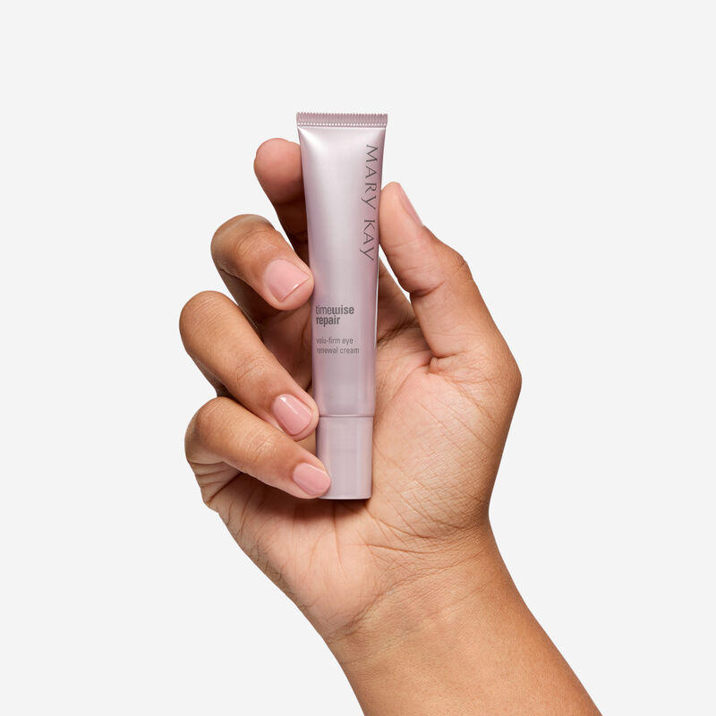 Mano de piel de tono medio sosteniendo el tubo de Eye Renewal Cream sobre un fondo liso