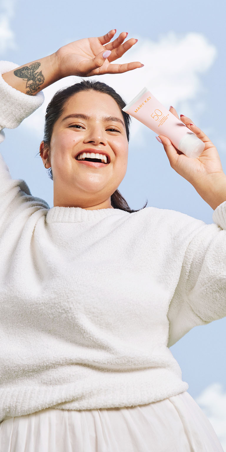 Modelo sosteniendo el Mary Kay Sunscreen Broad Spectrum SPF 50 bajo un cielo azul