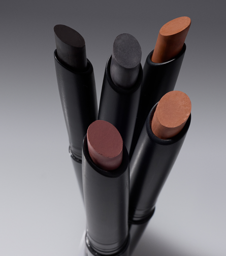 Five makeup contour sticks in assorted shades displayed in black tubes against a gray background.