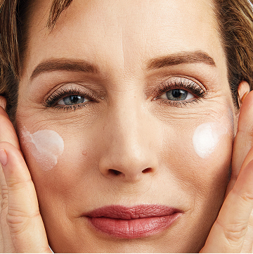 Mujer sonriendo a la c&aacute;mara aplic&aacute;ndose Mary Kay S&eacute;rum de Vitamina C+E en ambas mejillas