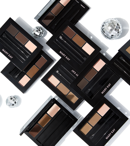 Mary Kay brow kits arranged in a flat lay, featuring multiple compact palettes with brow powders, highlighters, and applicators alongside mirrored disco ball accents.